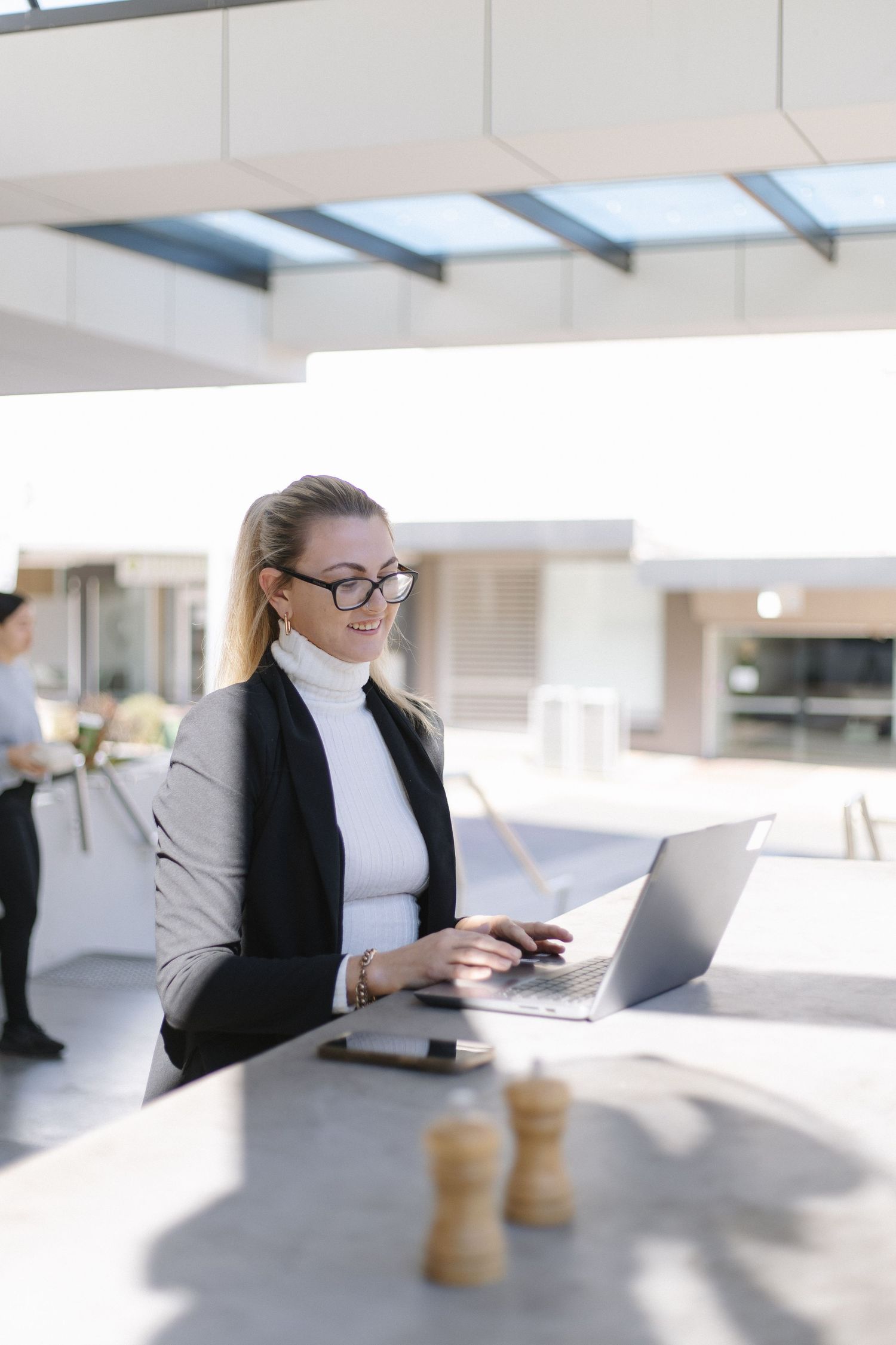Professional working at modern desk with laptop and coffee in bright office space.