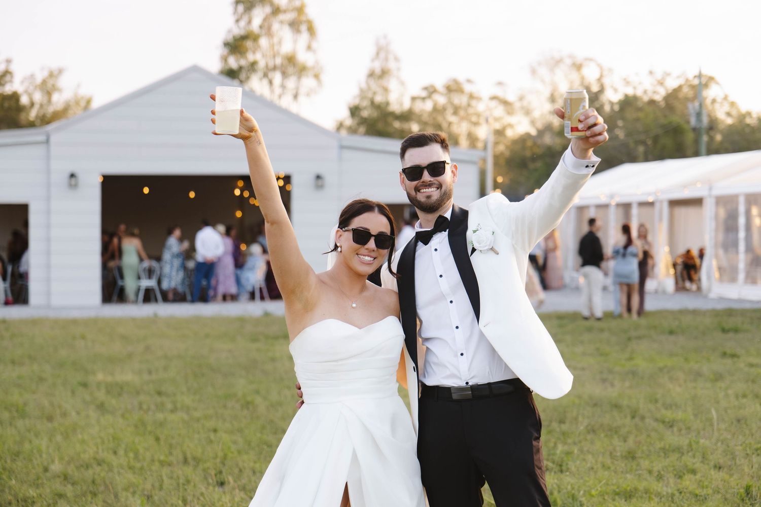 Newlyweds celebrate with raised arms outside a white reception venue on their wedding day.