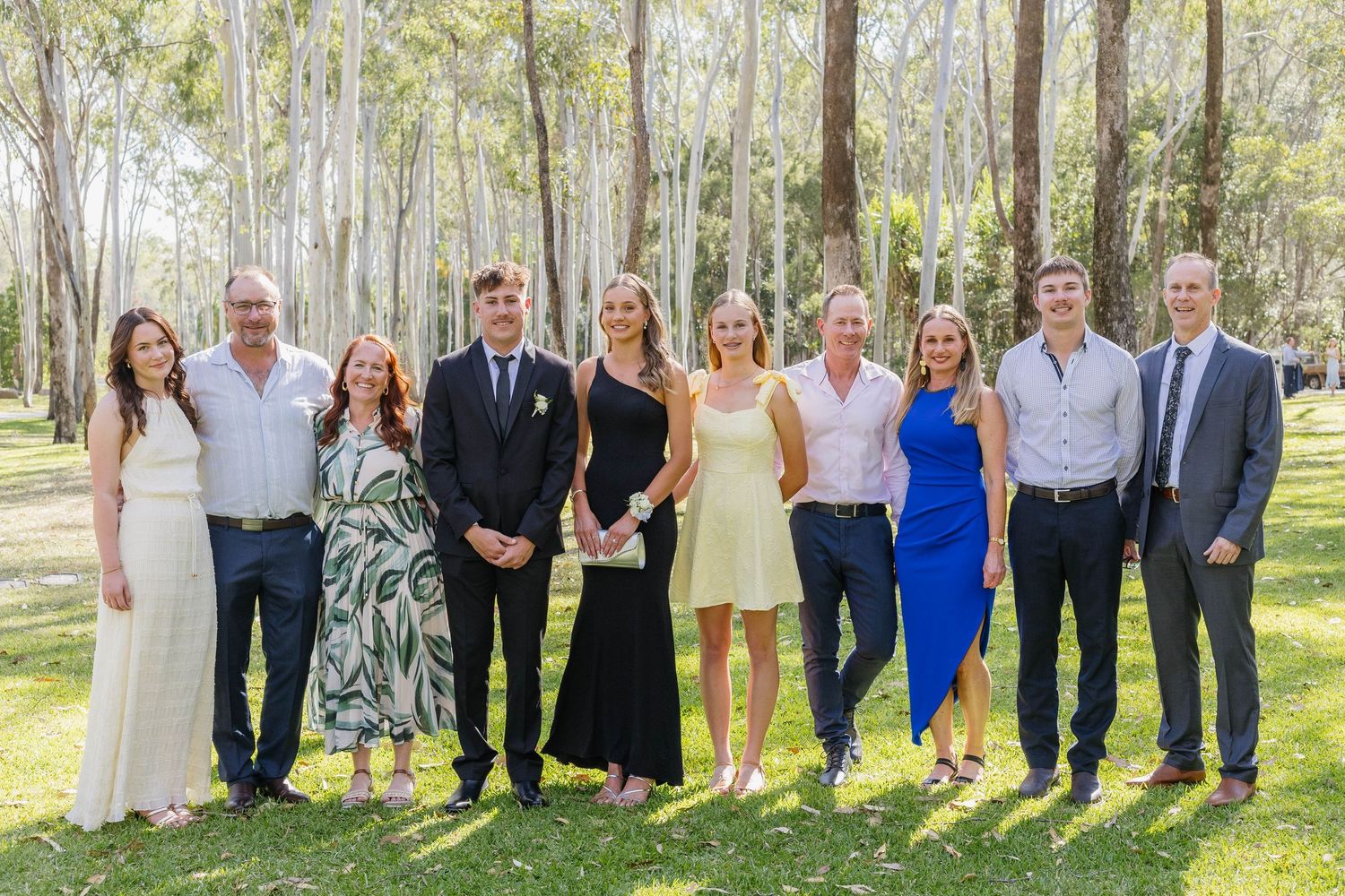 Large group photo of formally dressed people posing together in a eucalyptus grove.