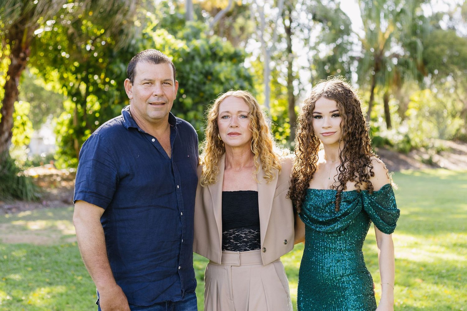 Group photo of people in formal attire standing together in a sunlit garden setting.
