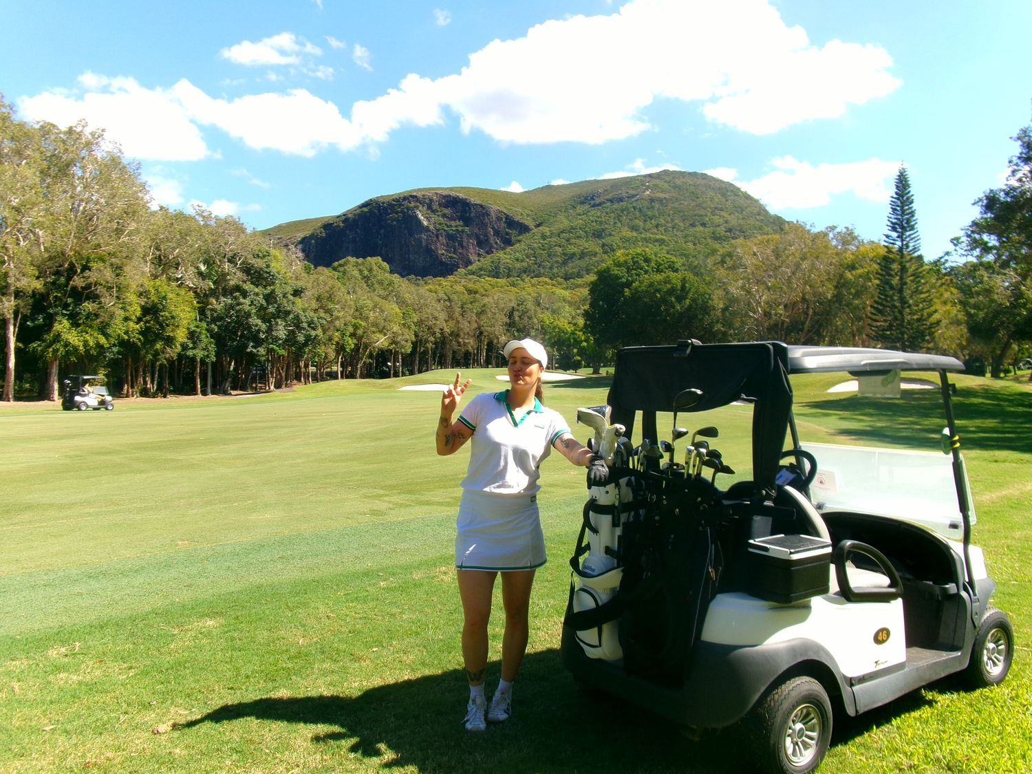 Golf course landscape with golf carts and players on rolling green hills under blue skies.