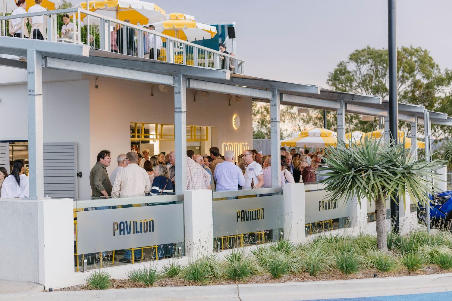 Exterior view of a modern restaurant patio with yellow umbrellas and outdoor seating.