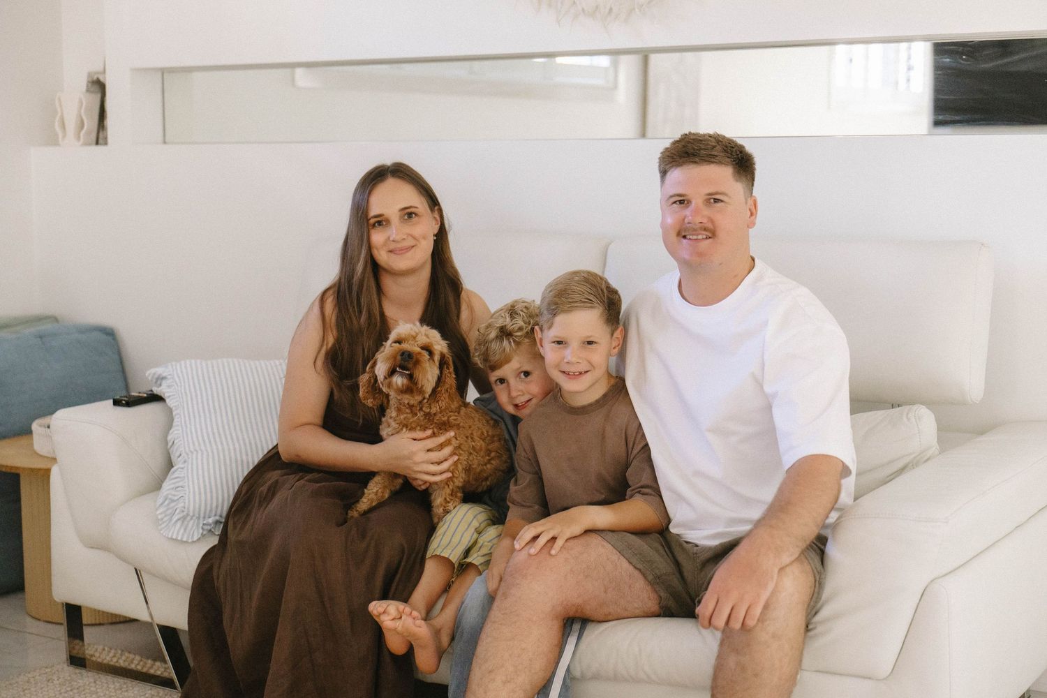 Family relaxing together on a white couch in a bright living room.