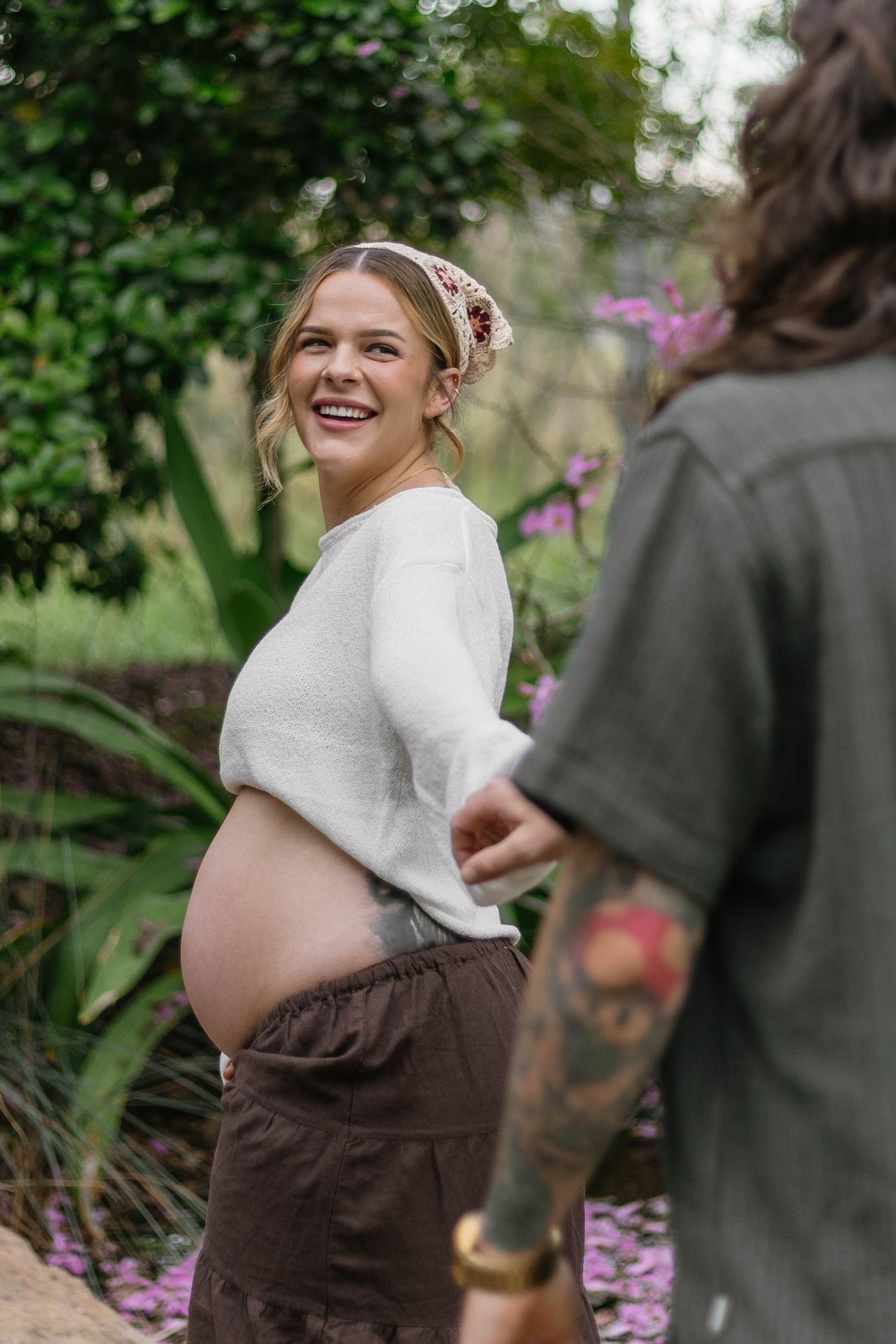 A maternity photoshoot in a garden setting with brown and white clothing.