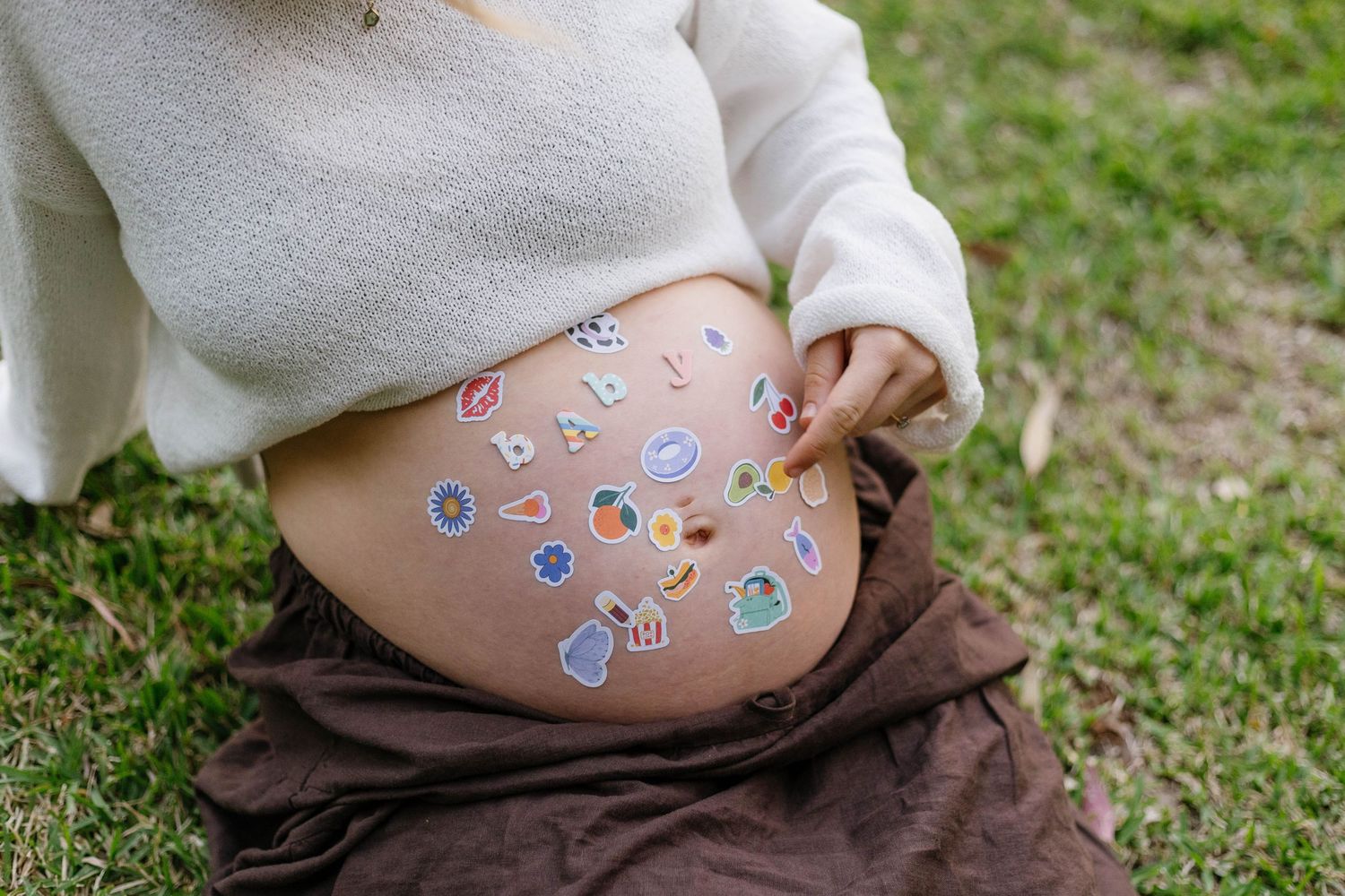 A pregnant belly adorned with colorful butterfly stickers in an outdoor garden setting.