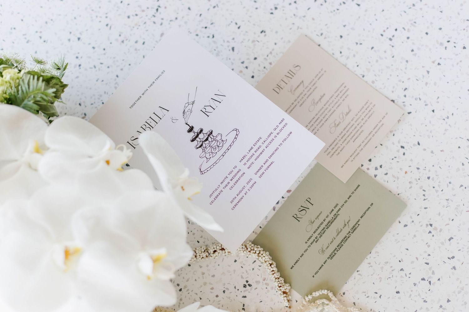Wedding stationery and floral elements displayed on a speckled white surface.