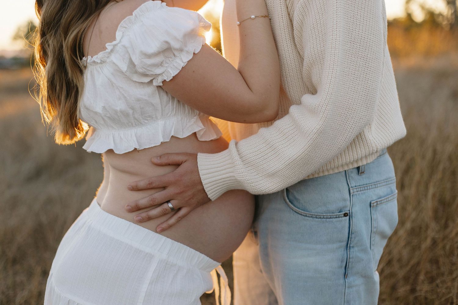 Romantic couple embraces in a sunlit field during golden hour.