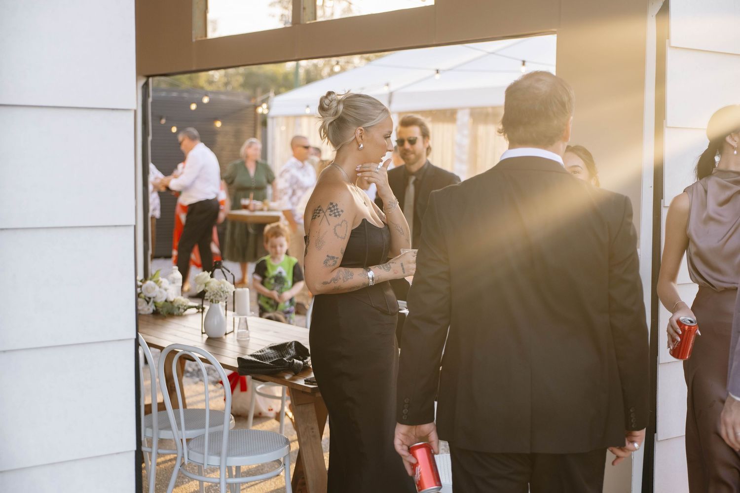 Wedding guests mingle during a sunset reception with warm lighting filtering through windows.