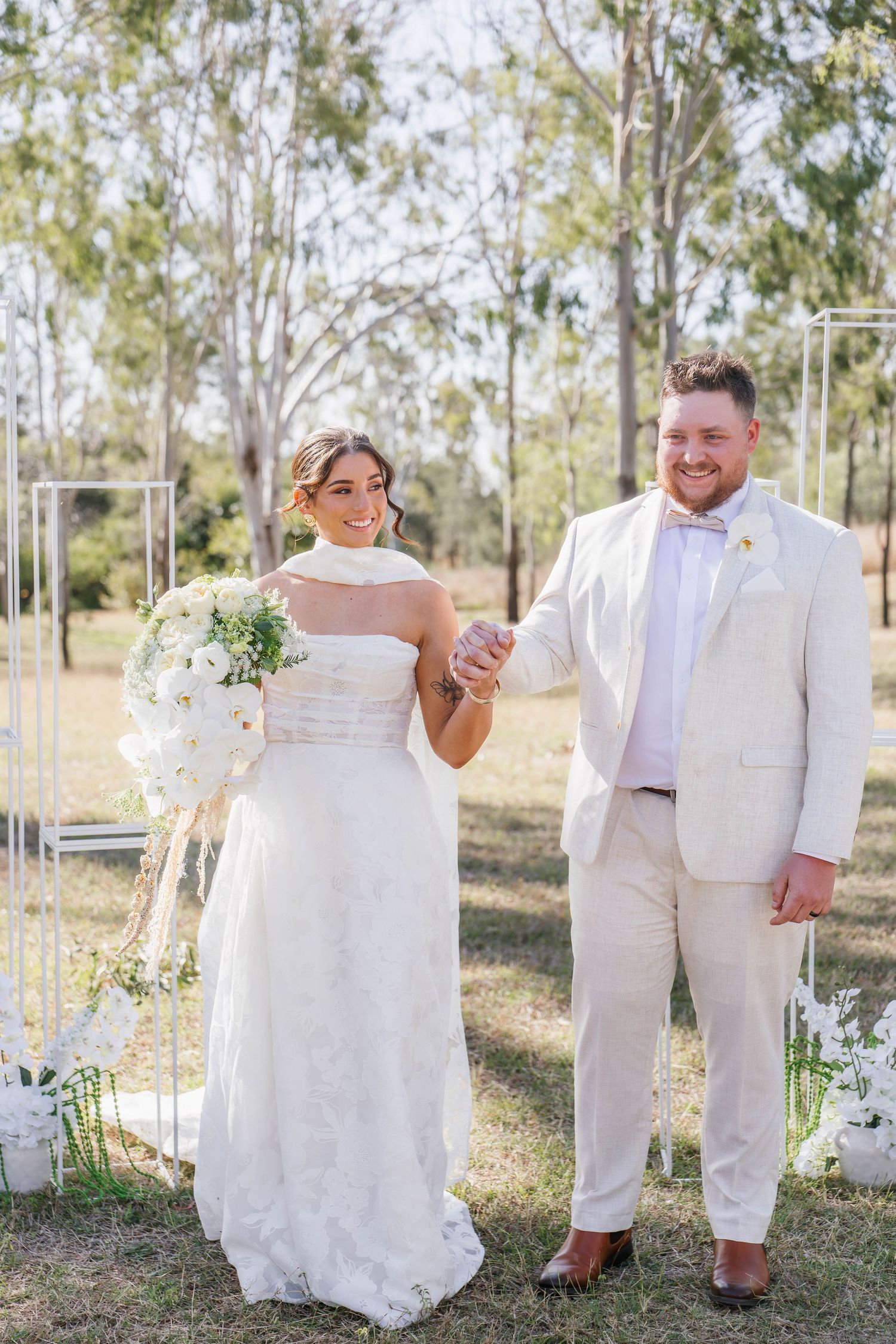 Wedding couple posing together in white attire against a natural outdoor backdrop.