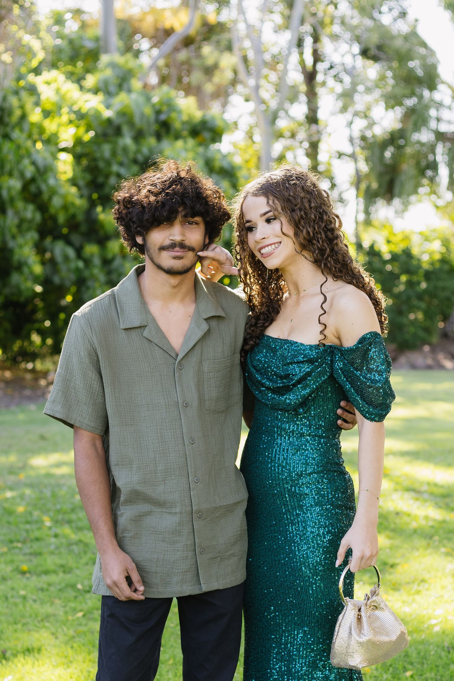 Couple in formal attire sharing candid moments in a sunlit outdoor setting.