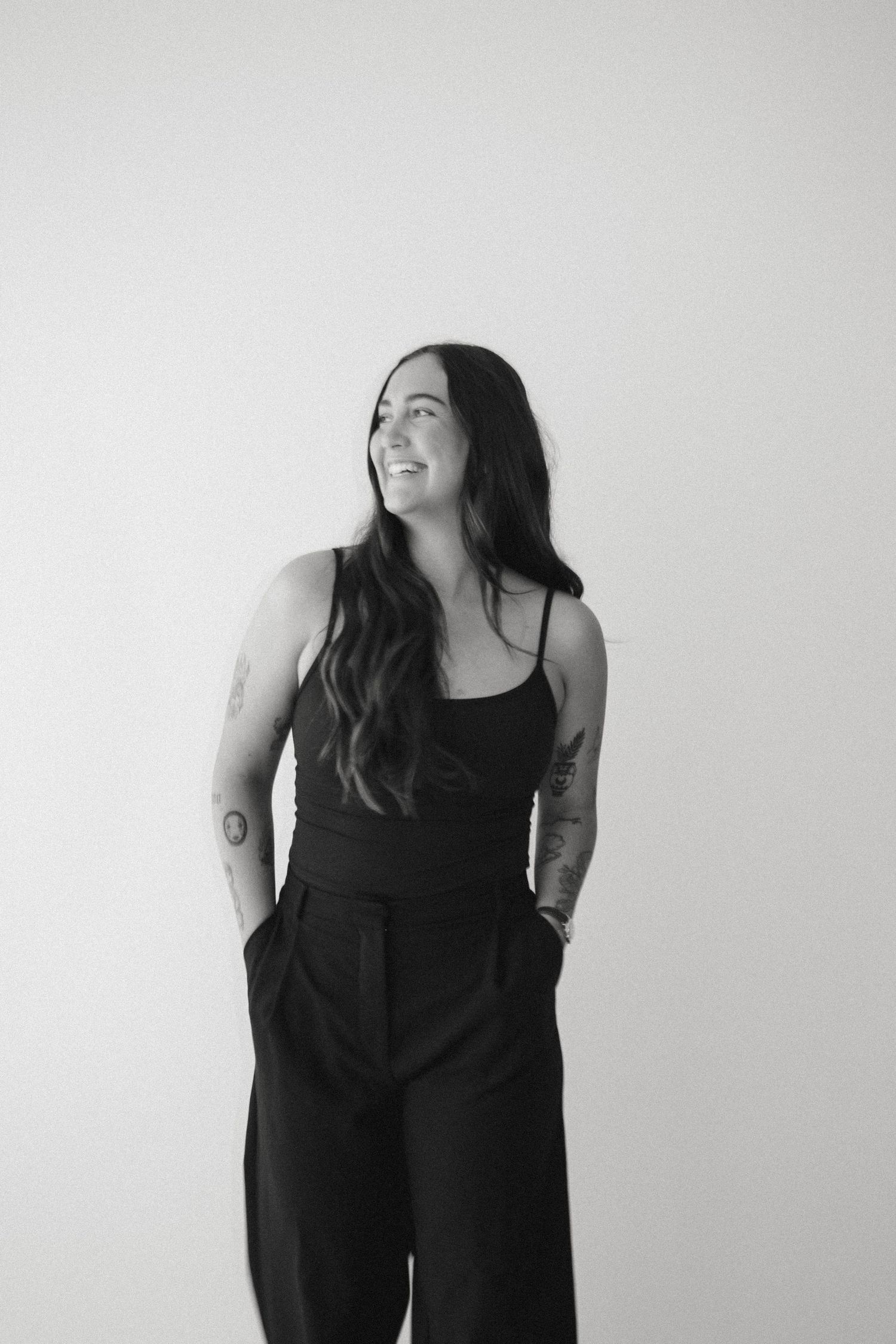 Black and white portrait of someone in a sleeveless top and wide-leg pants smiling against a light background.
