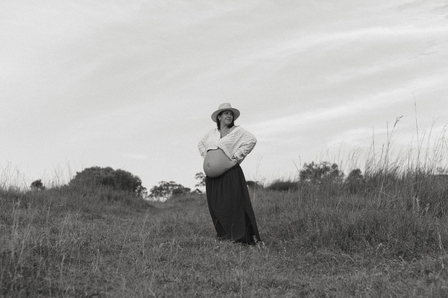 A series of five black and white photographs showing a person walking across a grassy hill against a cloudy sky.