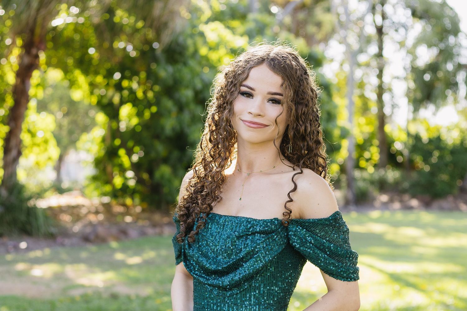 Woman in emerald sequin dress posing gracefully against natural outdoor backdrop.