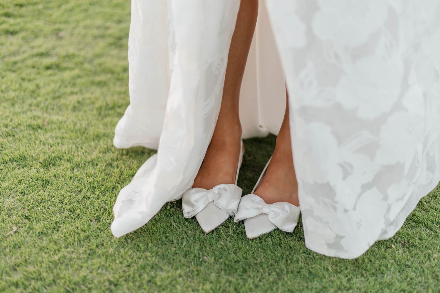 White bow detail on bridal shoes peeking out from under wedding dress hem.