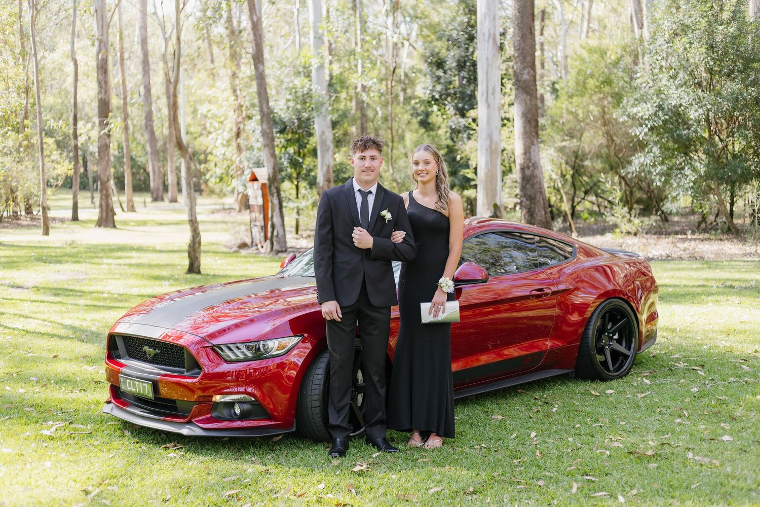 A red sports car parked on grass with formally dressed people posing beside it.