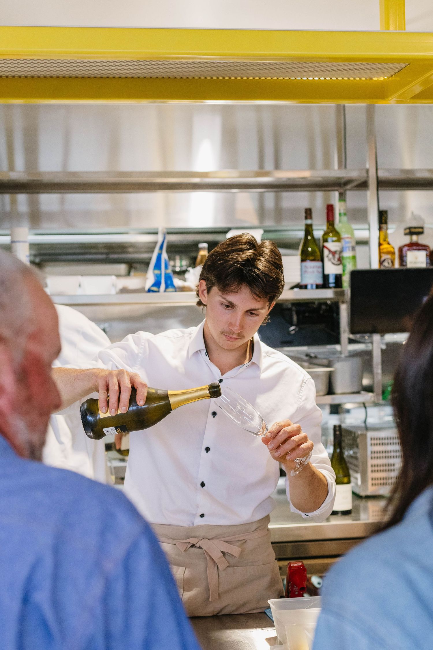 Staff member in white uniform pouring drinks at an upscale bar counter.
