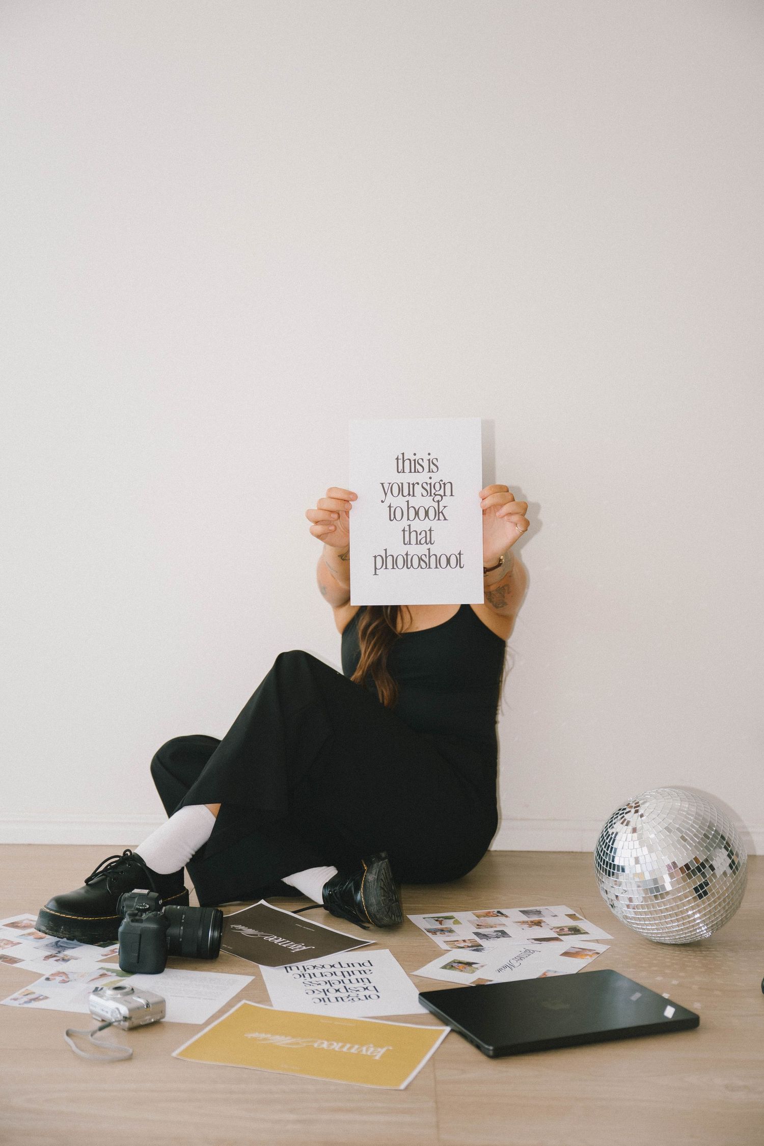 Artistic photo series showing person lying on floor holding white signs in different poses with disco ball and laptop nearby.