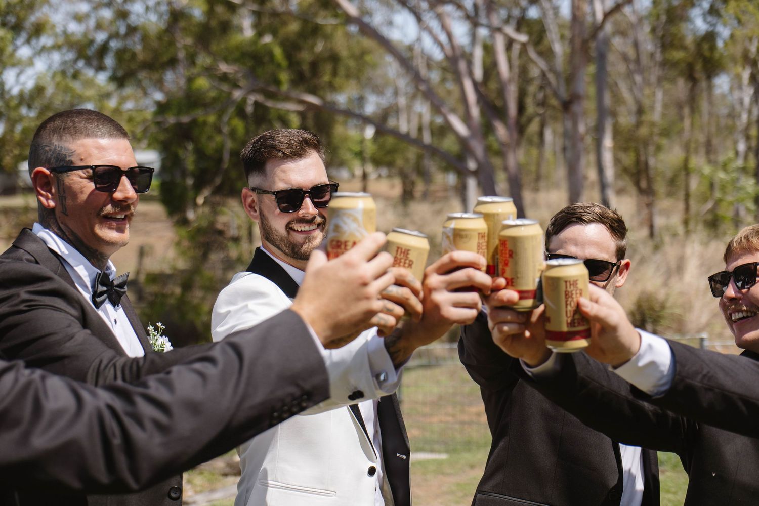 Groomsmen in sunglasses and black suits raising glasses for a celebratory toast.
