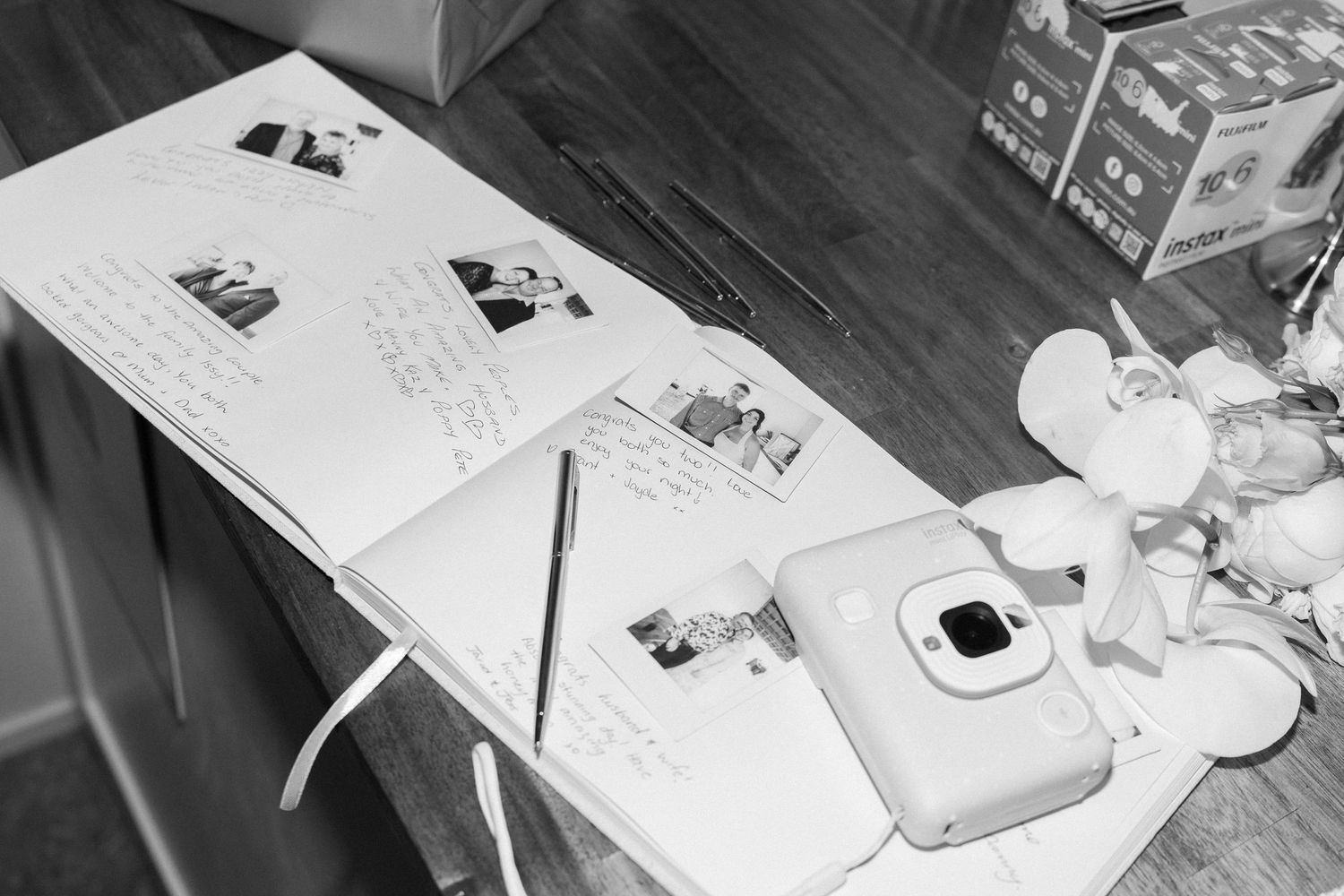 Black and white photo of wedding guest book and instant camera on dark table.