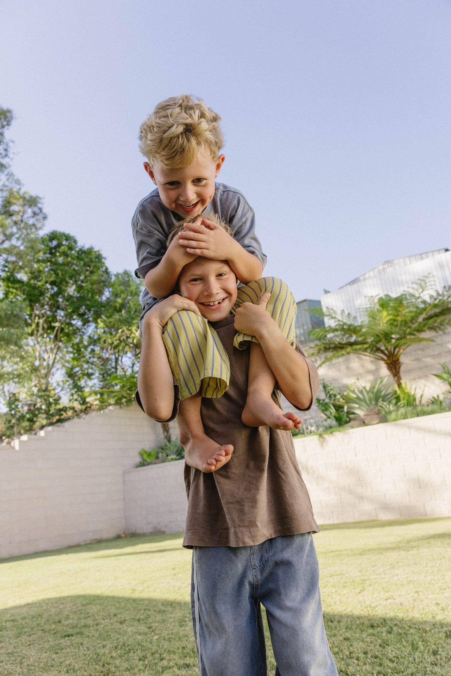Two kids playing and laughing together on green grass in a backyard.
