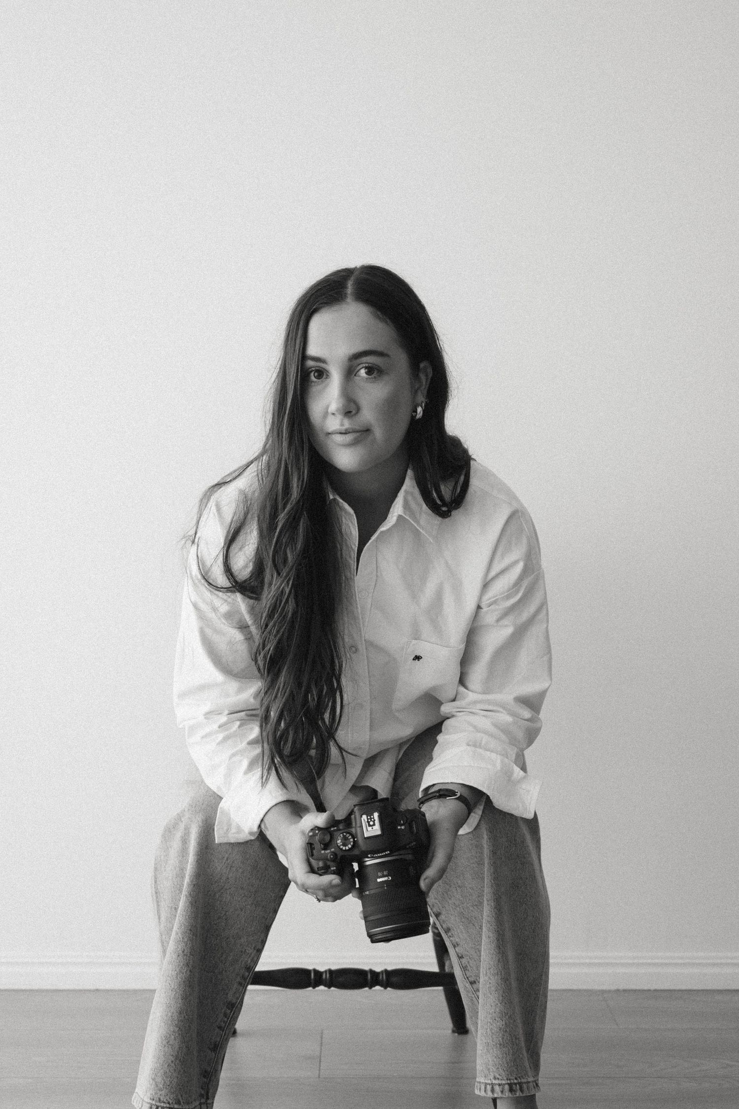 A photographer in a white shirt leans forward with a camera in a minimalist black and white setting.