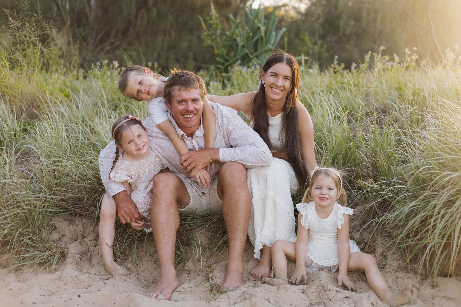 Group relaxing together on sandy beach dunes during golden hour.