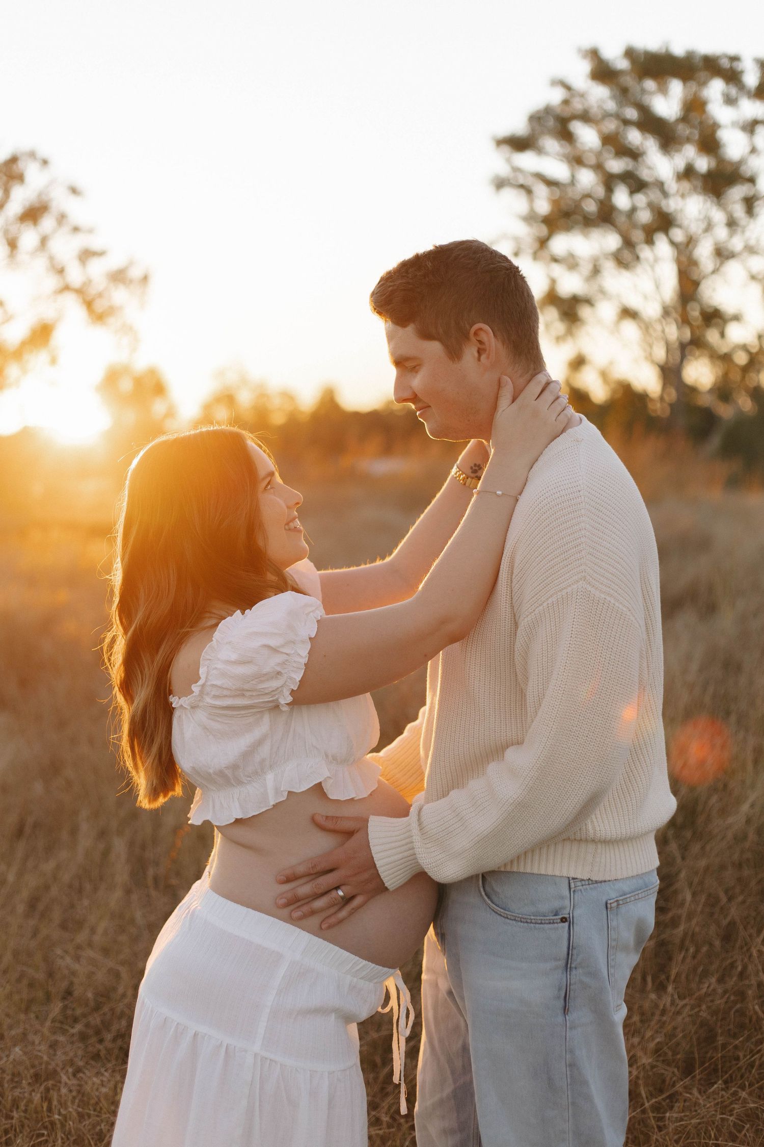 An intimate maternity portrait with warm sunset lighting in a field of tall grass.