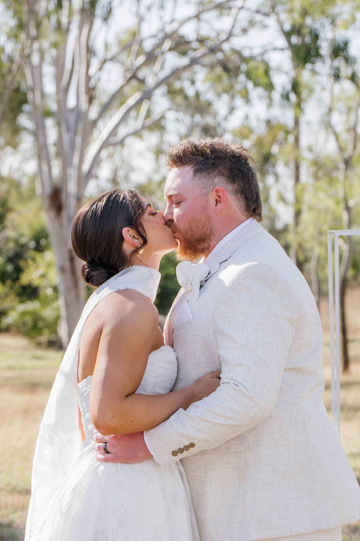 Intimate wedding portraits of couple in white attire embracing among eucalyptus trees.