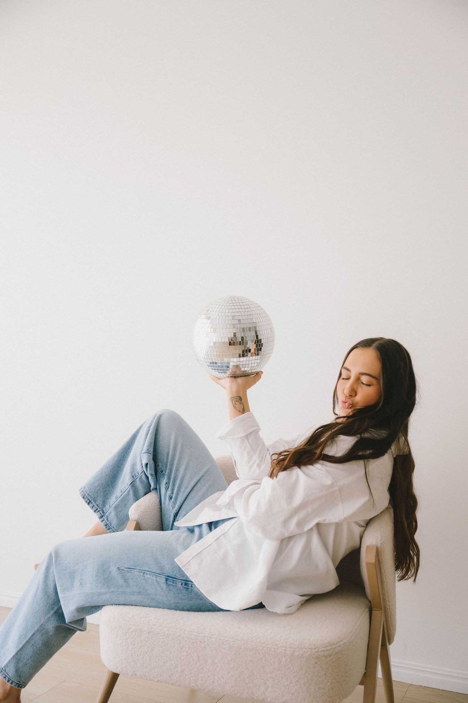 Person in white hoodie and blue jeans relaxing on white couch in minimalist setting.