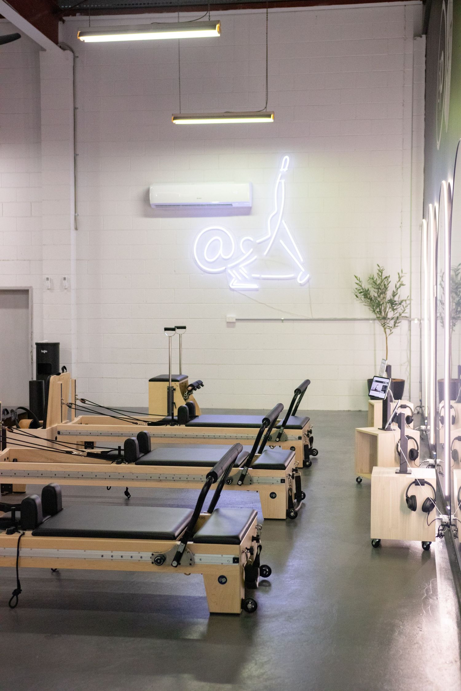 Clean modern fitness studio with multiple pilates reformer machines and neon lighting.