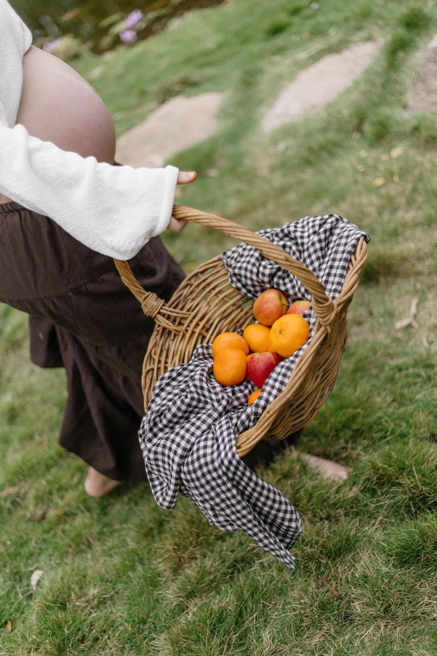 Wicker basket filled with fresh oranges on checkered cloth in garden setting.