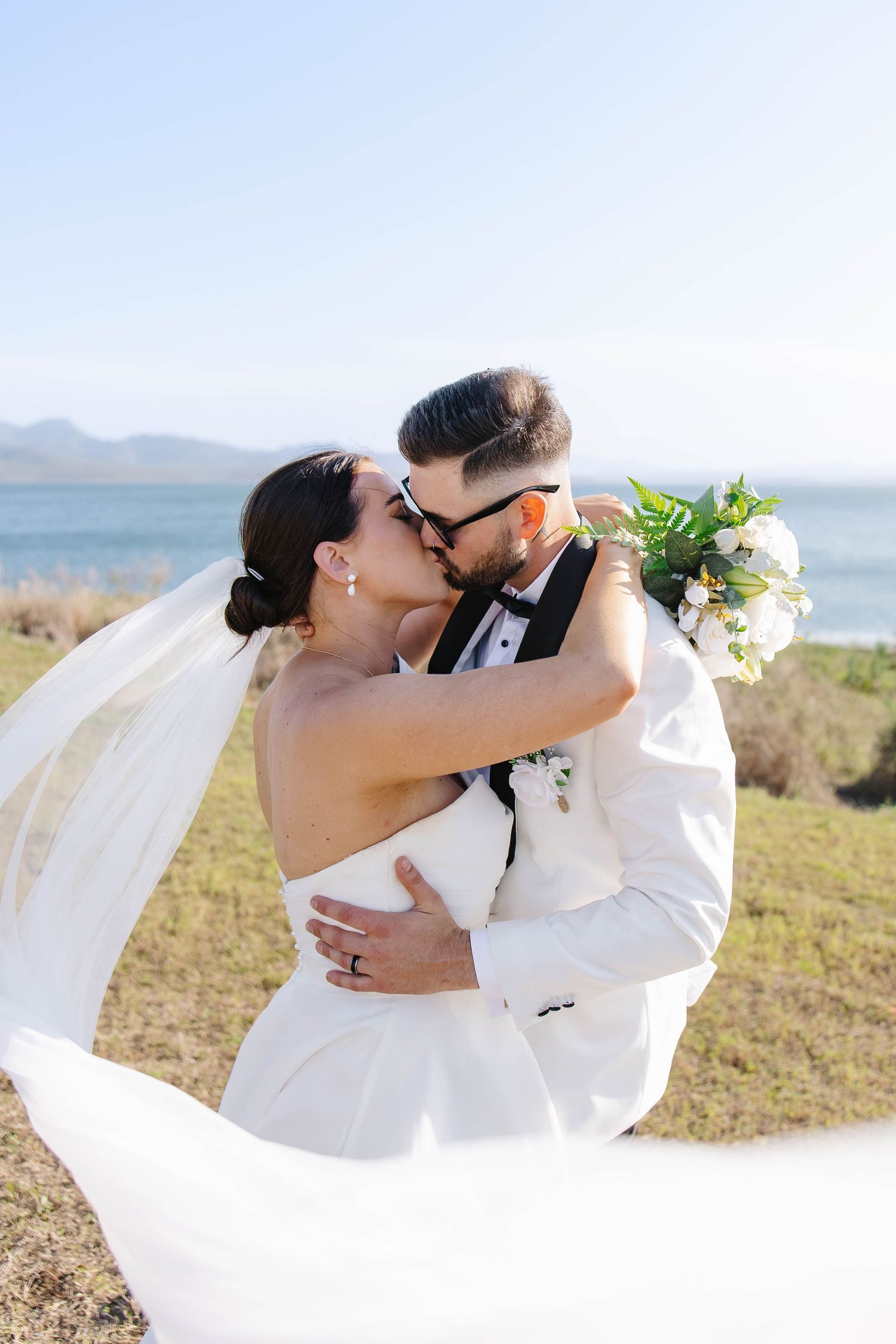 Romantic wedding portrait with flowing veil against coastal landscape.