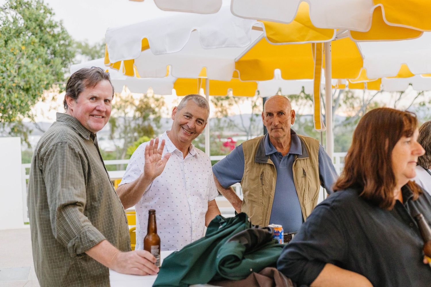 Guests mingling at an outdoor social event under yellow patio umbrellas.