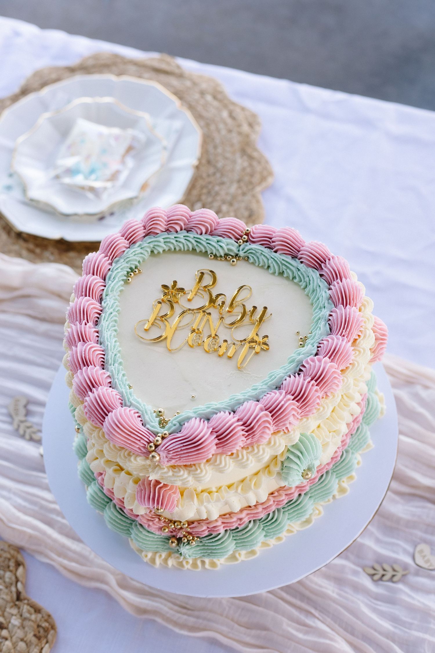 Heart-shaped cake decorated with pink and mint green piping and gold text.