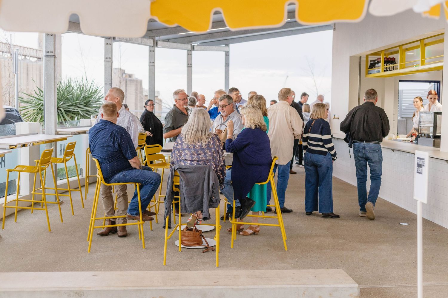 Wide view of a modern event space with guests and yellow accent furniture.
