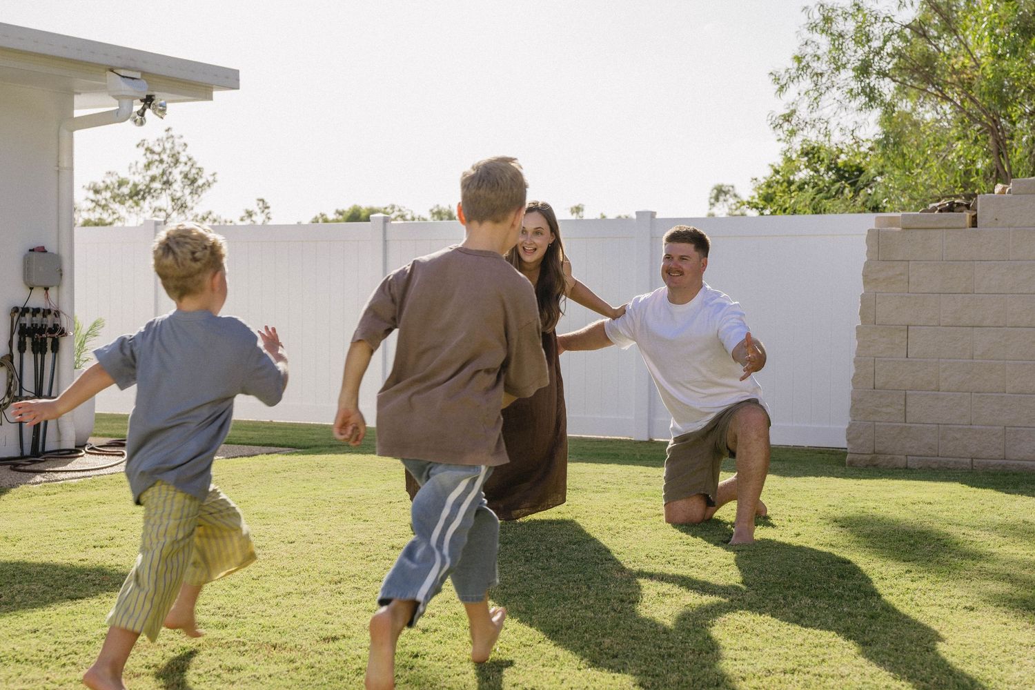 Active family playing and running together in a backyard with white walls.