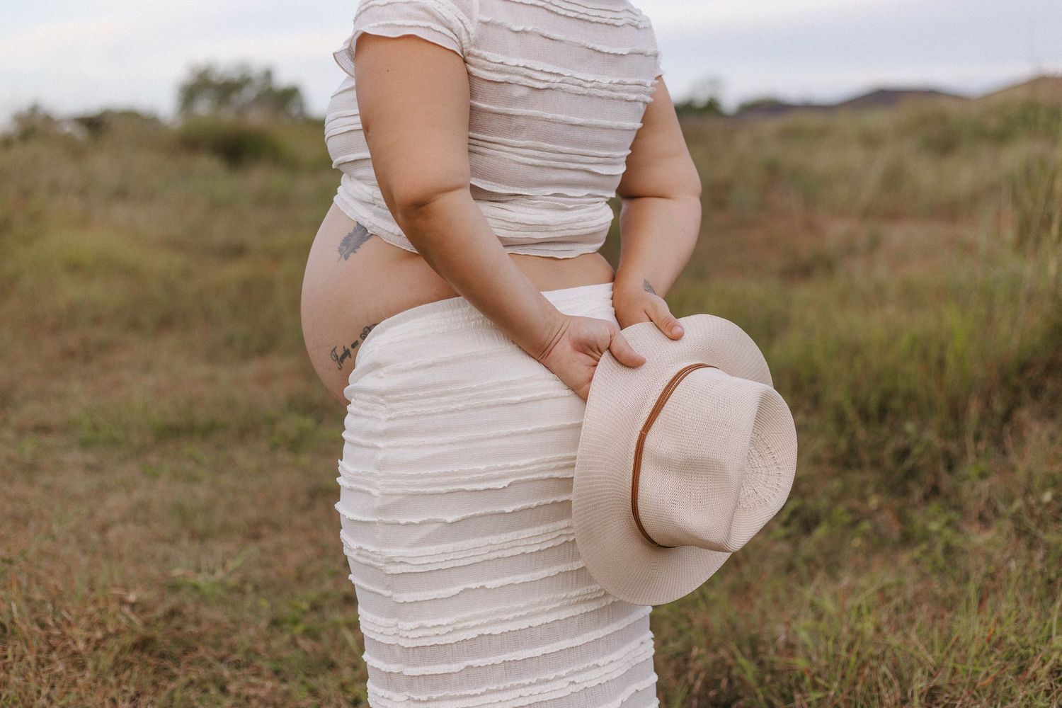 Person wearing a fitted cream-colored dress stands in a serene outdoor setting with tall grass.