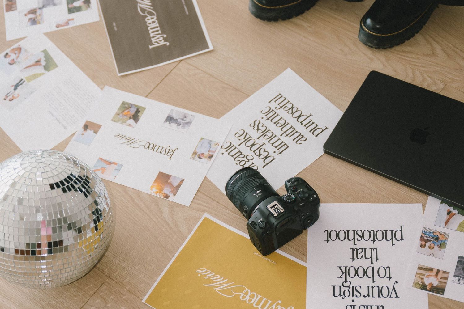 Flatlay of photography equipment and printed photos scattered on a wooden desk surface with natural lighting.