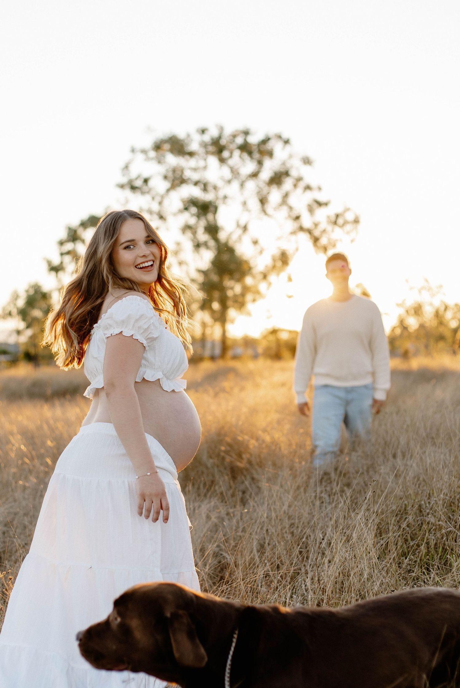 A white dress maternity photo session in a golden field at sunset.