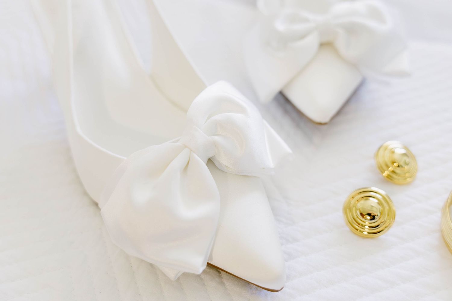 White silk ribbons and gold accessories arranged on a light neutral background.