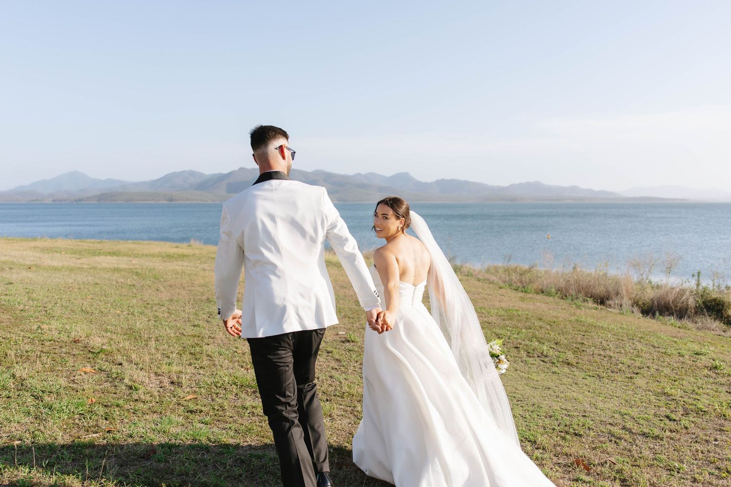 Wedding couple walking along coastal path with mountains and ocean in background.