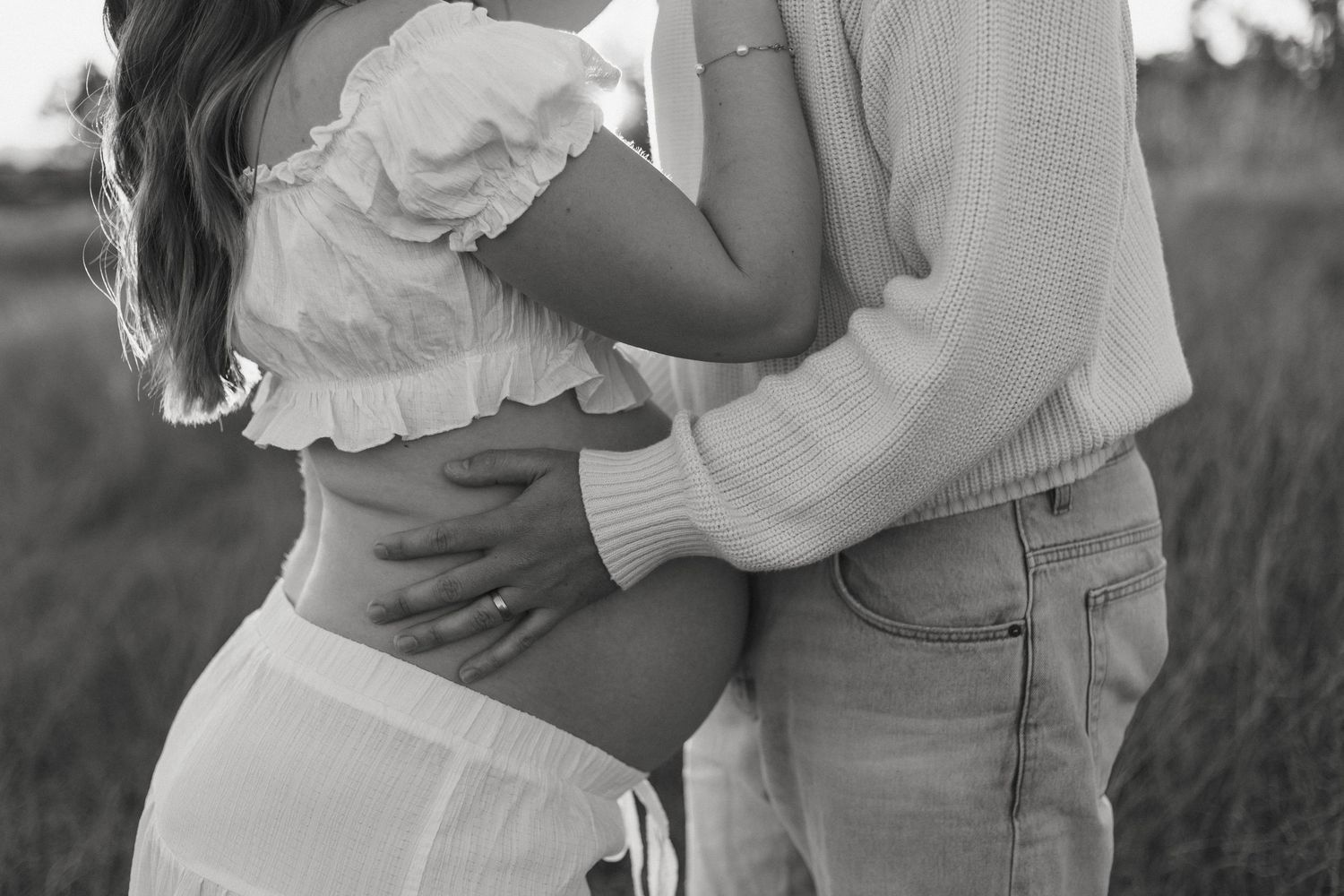 A black and white intimate maternity portrait in a field.