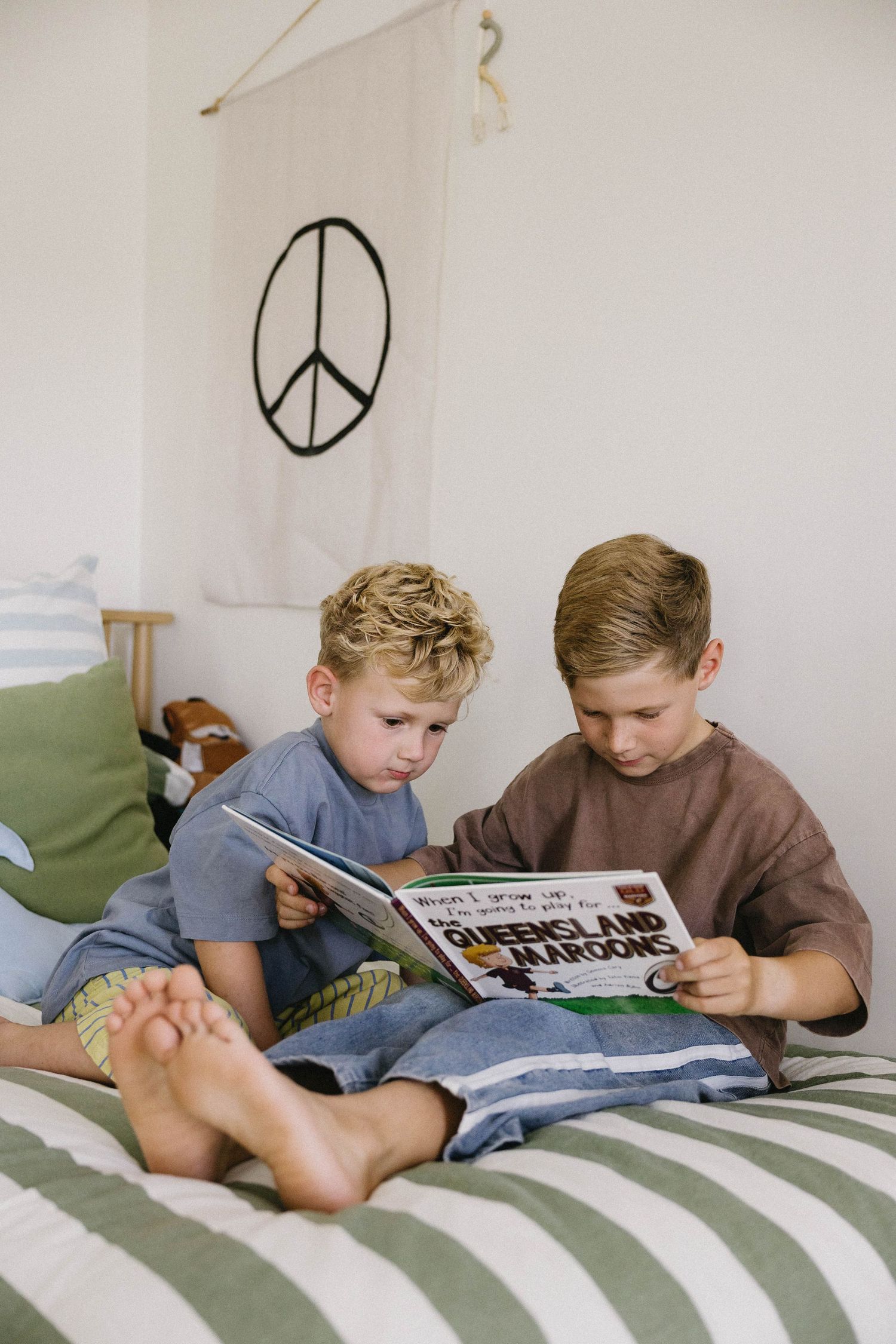 Two children reading together on a striped bedspread with peace symbol wall art.