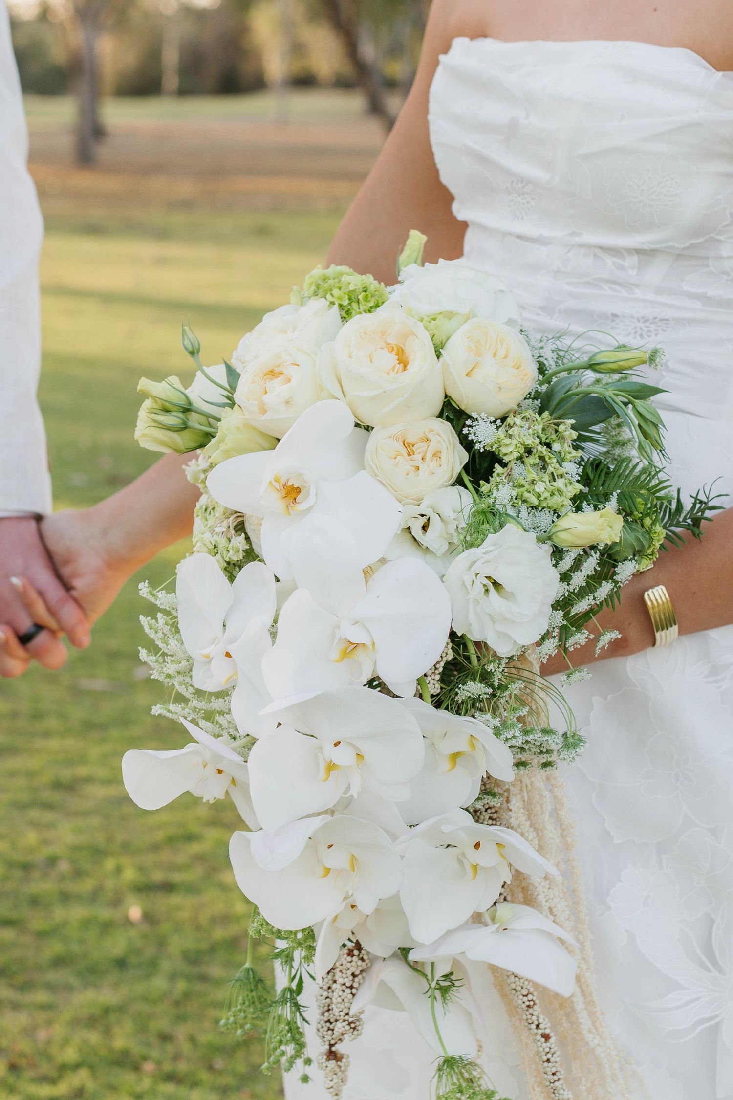 Elegant white orchid and peony bridal bouquet with cascading greenery.