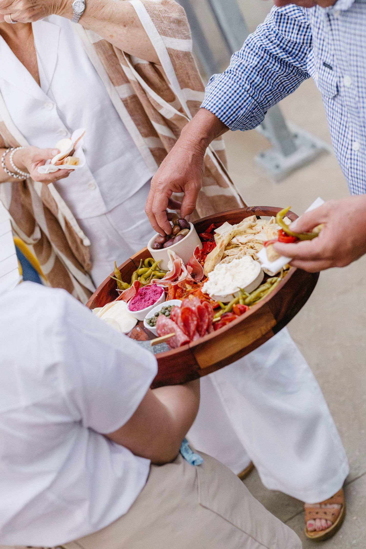 People serving themselves food from wooden platters at an outdoor gathering.