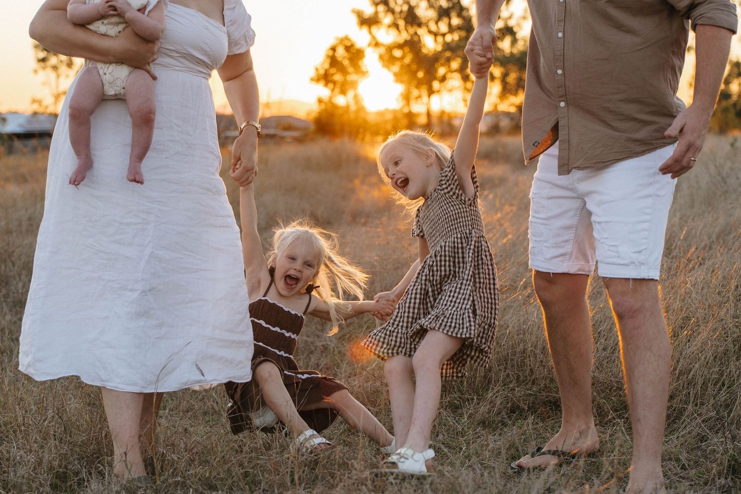 Playful family portraits captured in a grassy field at sunset.