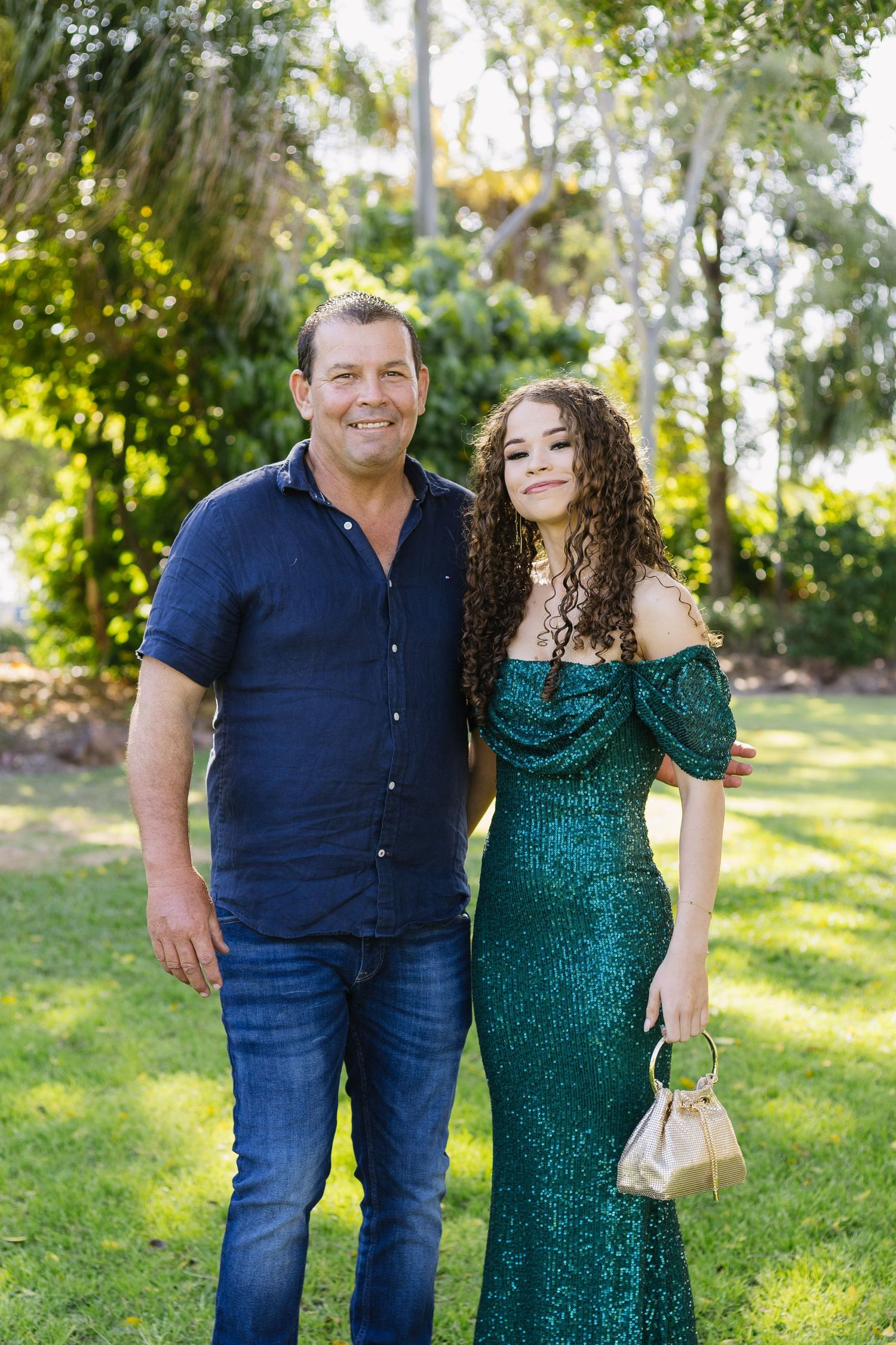 Couple in formal wear posing together in a sunny garden setting.