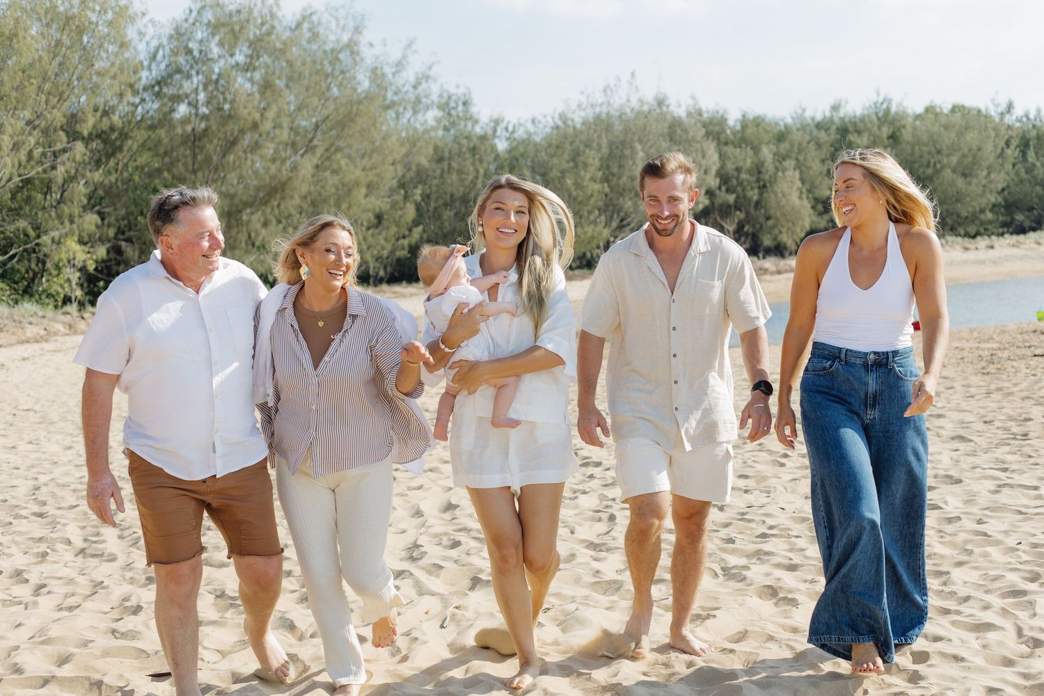 Group walking together on a sandy beach wearing coordinated light-colored casual outfits.