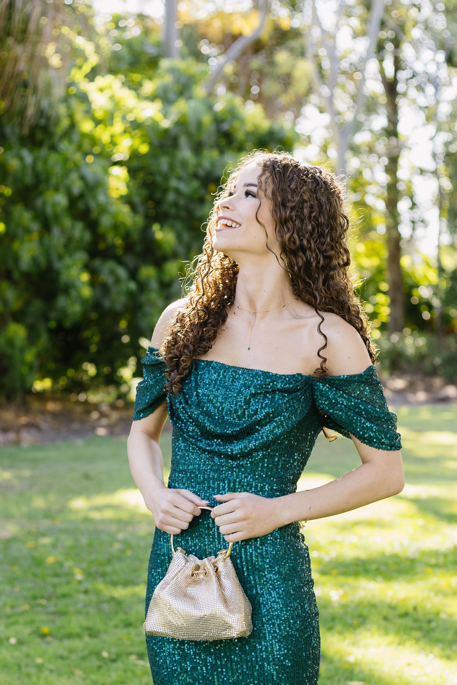 Woman in sparkling emerald dress posing joyfully in a garden setting.