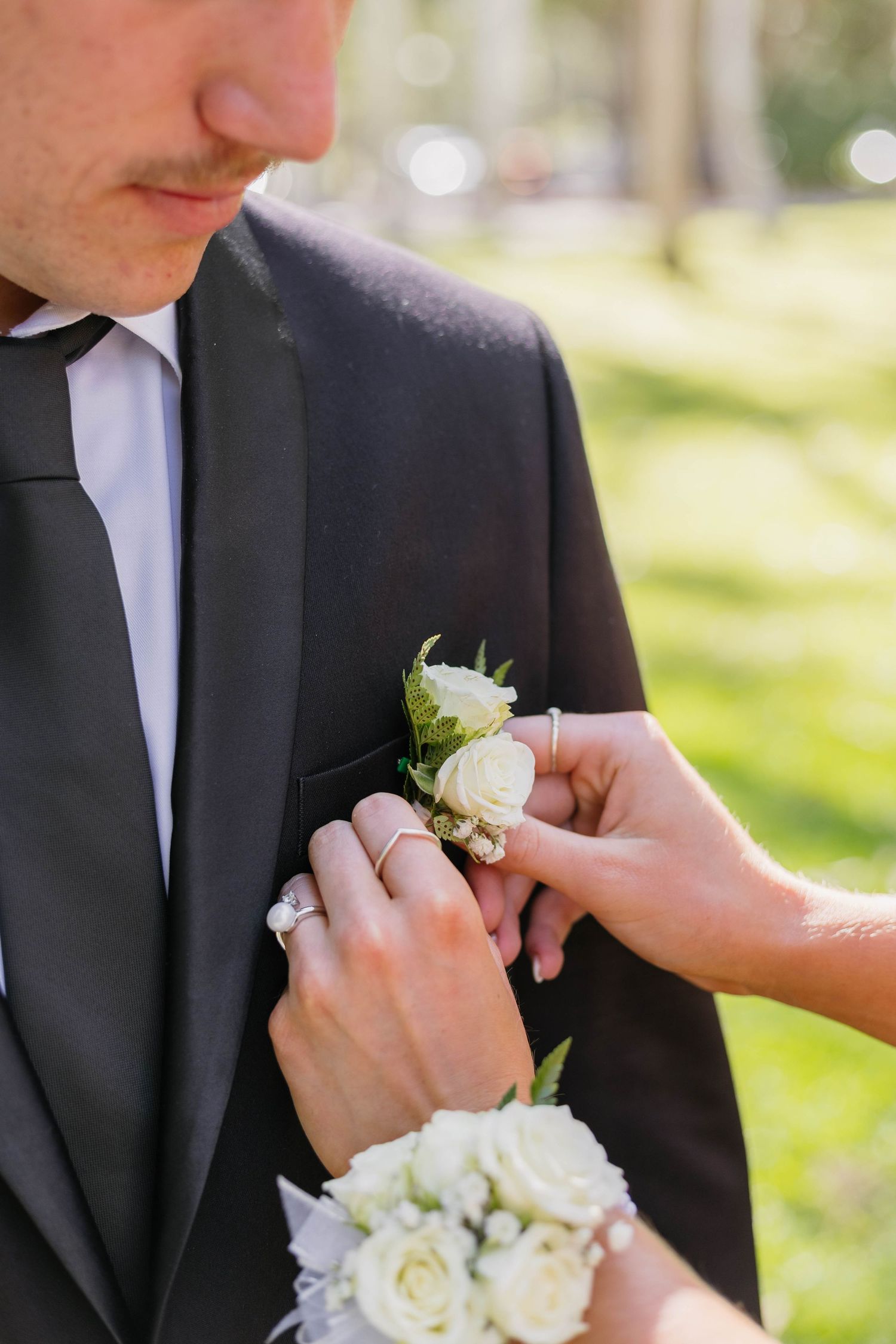 Close-up of hands pinning a white rose boutonniere onto a black suit lapel.